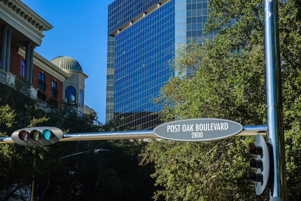"Post Oak Boulevard" street sign in downtown Houston, Texas with glass high-rises in background.